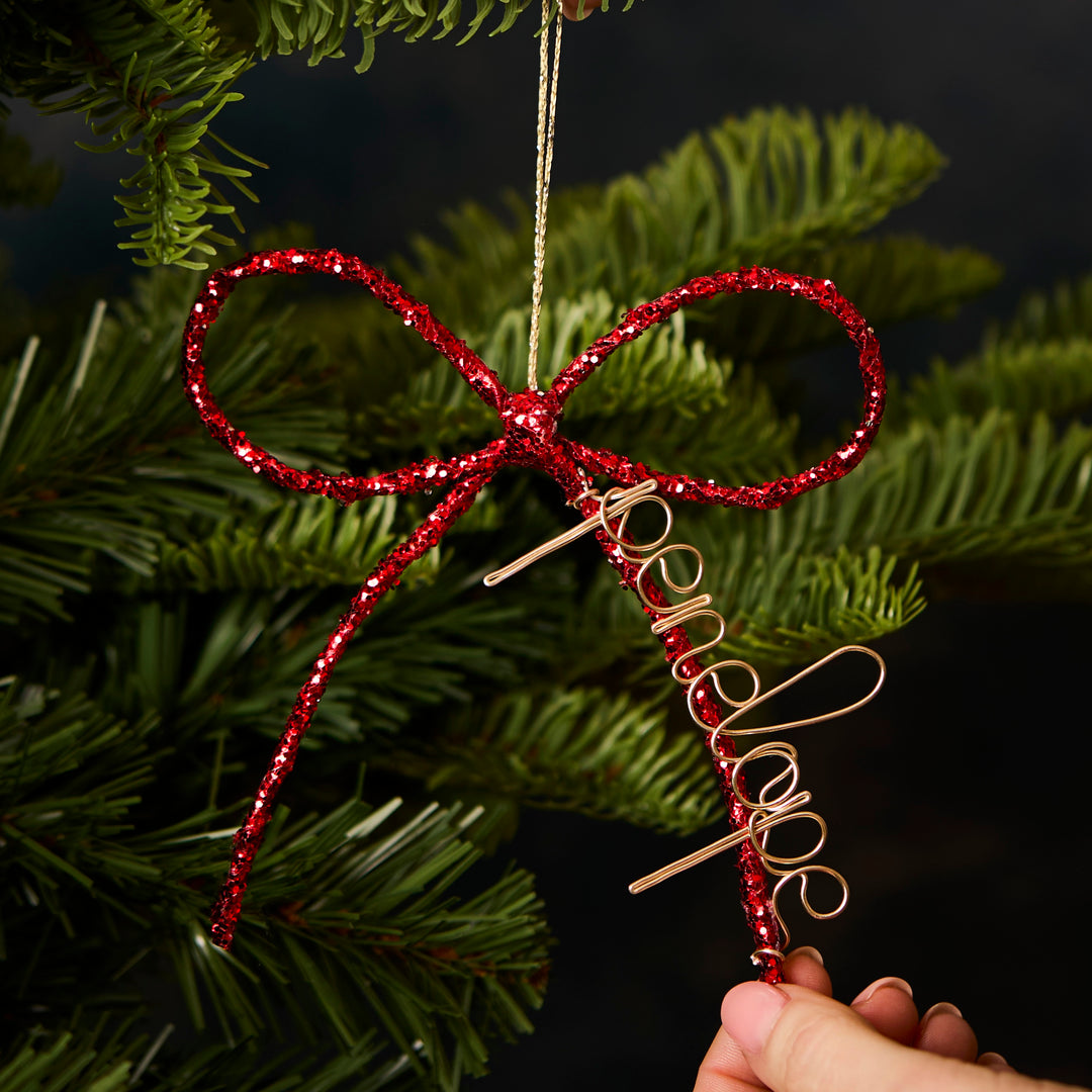 Red glittery bow ornament personalised with name 'Penelope' on a Christmas tree.