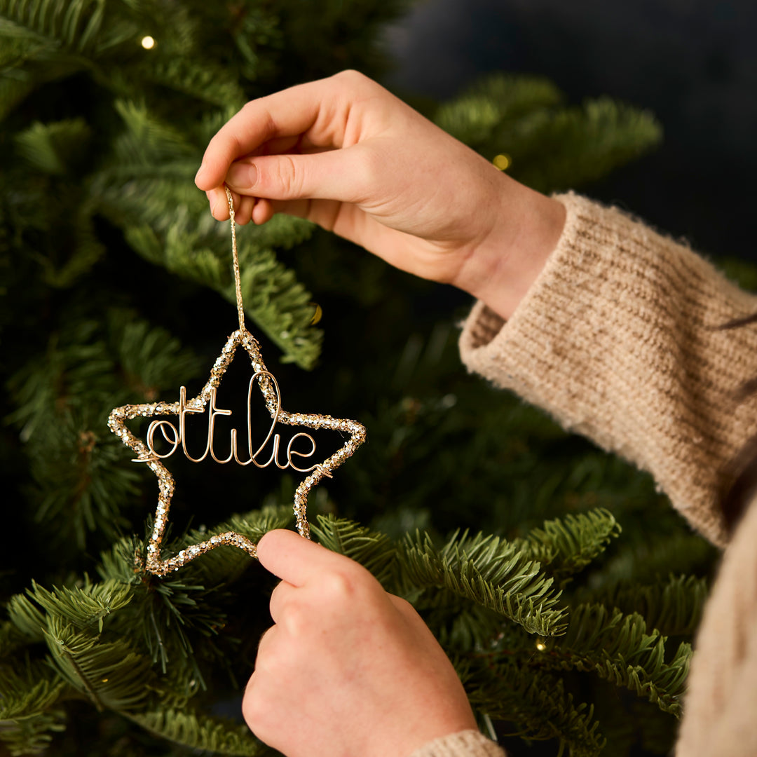 Star-shaped glitter Christmas ornament personalised with 'ottilie' being hung on a Christmas tree