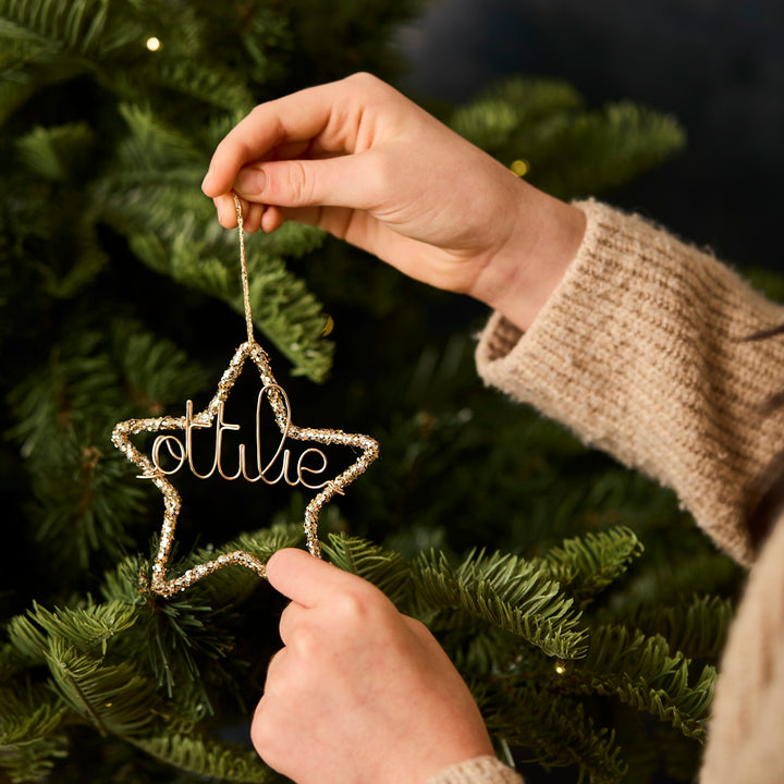 Star-shaped glitter Christmas ornament personalised with 'ottilie' being hung on a Christmas tree