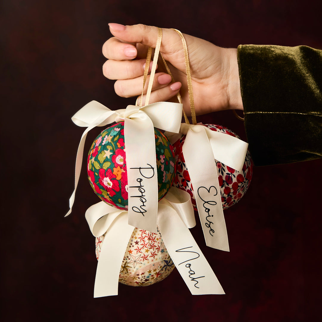 Hand holding three Liberty London fabric baubles with personalised ribbons 