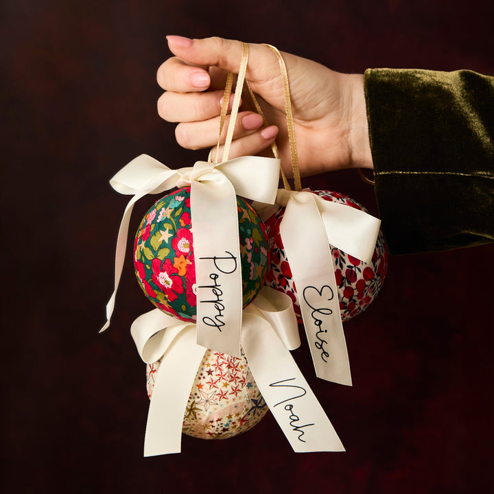 Hand holding three Liberty London fabric baubles with personalised ribbons 