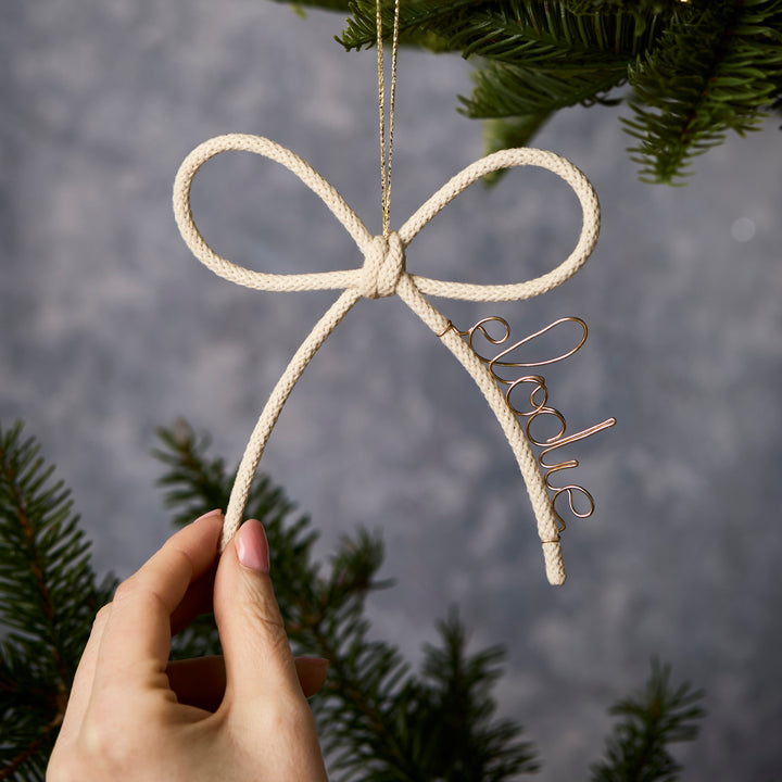 Hand holding a Christmas white knit bow ornament with personalised with name  'Elodie' on a blurred natural background