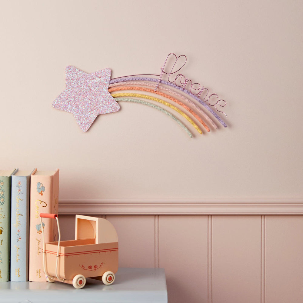 a pink star-shaped decoration hanging on a pink wall, with a pink stroller and books on a shelf below it.